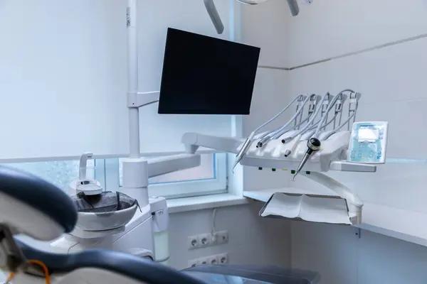Bu görüntüde yüksek teknoloji koltuğu, monitörleri ve etkin diş tedavisi ve hasta bakımı için düzenlenmiş aletleri olan çağdaş bir diş muayenehanesi yer alıyor..