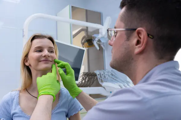 Görüntü modern bir klinikte bir diş hekimini gösteriyor. Hastaların yüz bölgesini inceliyor. Gelişmiş diş teknolojisiyle düzenli ağız sağlığı değerlendirmelerinin bir parçası olarak konfor sağlıyor..