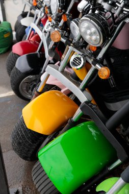 Otoparktaki renkli küçük motosikletlerin yakın çekim görüntüsü. Evet. Çarpıcı sarı ve yeşil çamurluklar canlı renklerin arasında duruyor, eğlenceli ve maceracı bir hava sergiliyorlar..