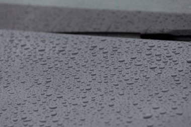 Bu resim, etrafındaki dokularla birlikte her damlacığın karmaşık detaylarını vurgulayan, karanlık bir yüzey üzerinde dinlenen su damlacıklarının makro perspektifini içerir..