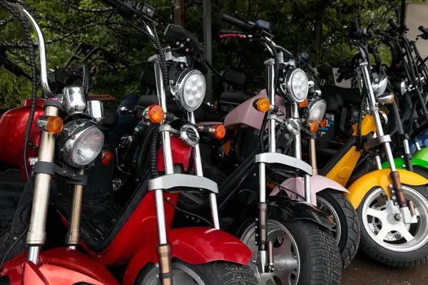 Bu resim, her biri eşsiz farlarla donatılmış canlı renkli scooter koleksiyonu sergiliyor. Açık hava ortamının ortasındaki şık tasarımlarını gözler önüne seriyor..