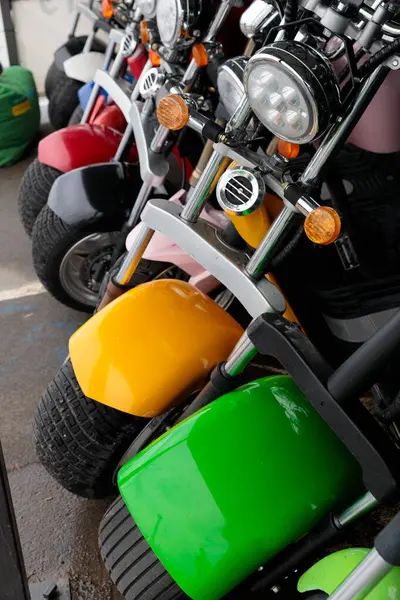 Otoparktaki renkli küçük motosikletlerin yakın çekim görüntüsü. Evet. Çarpıcı sarı ve yeşil çamurluklar canlı renklerin arasında duruyor, eğlenceli ve maceracı bir hava sergiliyorlar..