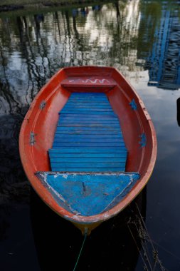 Bu resim, sakin sularda yüzen parlak turuncu bir tekne, çevreyi güzel yansıtıyor, sükuneti ve doğayı barışçıl bir şekilde kucaklıyor..