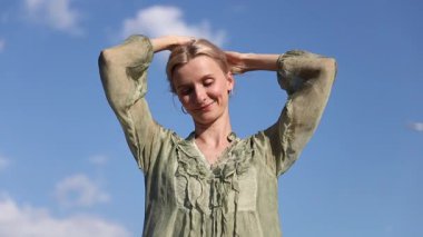 Uzun saçlı neşeli bir insan açık yeşil bir bluz içinde güneşli bir günde neşe ve pozitiflik saçan güzel mavi bir gökyüzüne karşı poz verir..