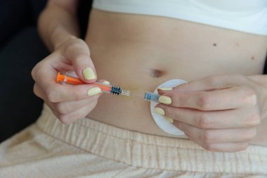 Görüntü, karnına iğne yapmaya hazırlanan bir kişinin ellerini yakalıyor. Şırınga ve pamuk pedi vurguluyor, sağlık ve öz bakım konularını vurguluyor..