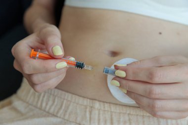 Bu resim, elinde şırınga tutan ve evde rahat bir ortamda titiz bir sağlık yönetimi uygulaması sergilerken enjeksiyona hazırlanan bir kişiyi gösteriyor..