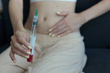 Görüntü, bir insanın elinin şırıngayı kavraması, midesinin üzerinde durması, kişisel sağlık yönetimi ve kendi kendini idare etmenin önemini simgeliyor..