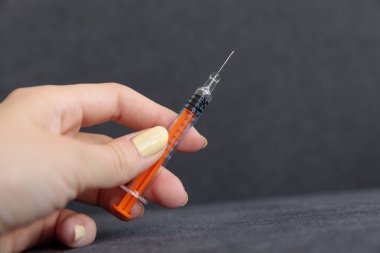 Bu resim, şırıngayı portakal pompasıyla tutan bir elin yakın plan görüntüsünü içeriyor. Siyah bir arka fona karşı şeffaf namludaki artışları ve ölçümleri gösteriyor..