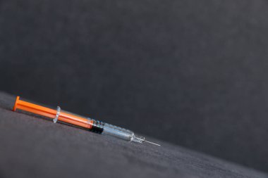 Görüntü karanlık bir arka plana yatay olarak yerleştirilmiş tıbbi bir şırınga gösteriyor. Aşılama ve sağlık prosedürlerinin modern tıptaki önemini vurguluyor..