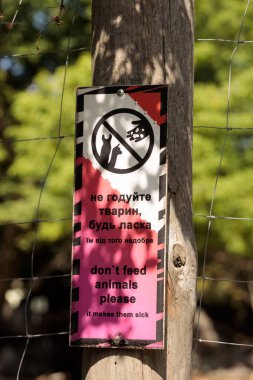 Görüntü birden fazla dilde bir işaret içeriyor, ziyaretçileri hayvanları beslememeleri konusunda uyarıyor, onları beslemenin onları hasta edebileceğini vurguluyor, grafik çizimlerle vurguluyor..