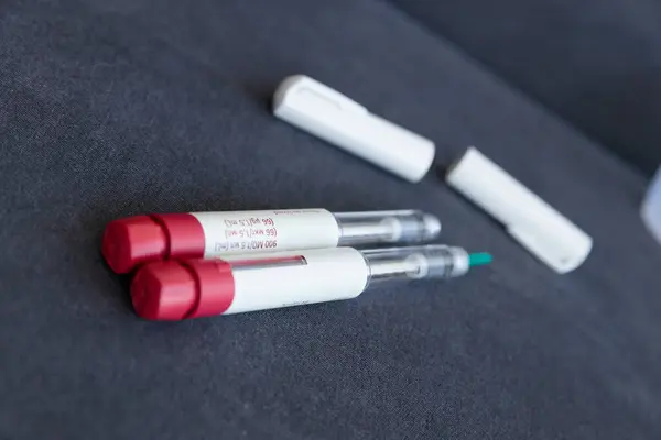 Bu resim iki tıbbi insülin kalemini kırmızı başlıklarla belirgin bir şekilde gösteriyor, açık rezervlerini koyu gri arkaplanla birlikte yakın çevredeki beyaz koruyucu başlıklarla vurguluyorlar..