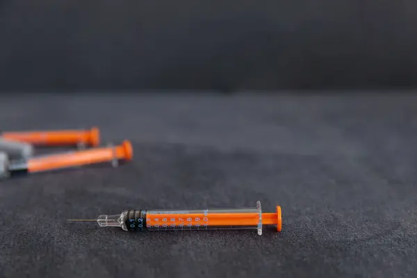 Bu resim, turuncu başlıklı şırıngaların yakın çekimini ve onların karmaşık detaylarına odaklanmayı gösteriyor, karanlık bir arkaplan üzerine kurulmuş, eğitim veya sağlık hizmetleri görselleri için mükemmel..