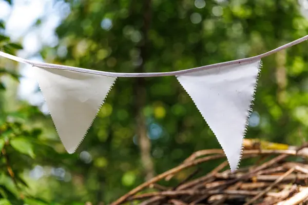 İki beyaz üçgen bayraklar yemyeşil bir ortamda bir ipten sarkıtılır. Çevreyle güzelce harmanlanırlar ve açık hava koşullarını güçlendirirler..