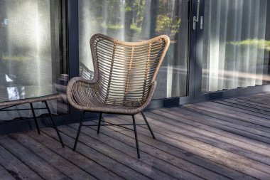 Görüntü, ahşap bir güverteye yerleştirilmiş güzel tasarlanmış bir rattan sandalyeyi sergiliyor, yanında da cam bir masa, aydınlatmalı modern açık havada yaşam..