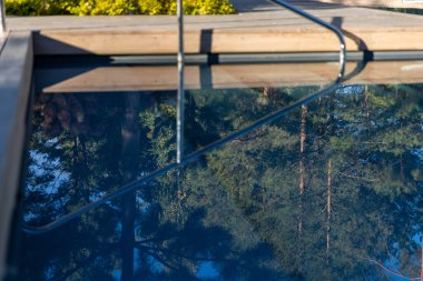 Bu görüntü güzel bir şekilde çevredeki yeşillikleri ve ağaçları yansıtan huzurlu bir havuzu sergiliyor. Rahatlamak ve doğanın tadını çıkarmak için mükemmel sakin bir atmosfer yaratıyor..