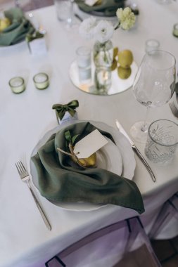 Yeşil peçeteler, dekoratif eşyalar, cam eşyalar ve taze çiçekler ile güzel düzenlenmiş bir yemek masası misafirler için sofistike ve davetkar bir ortam yaratıyor..