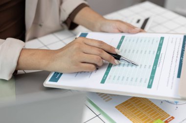Bir kişi bütçe tablosunu işaret ediyor. Çarşaf yeşil ve beyaz ve üzerinde bir sürü rakam var. Kişi numaraları göstermek için bir kalem kullanıyor.