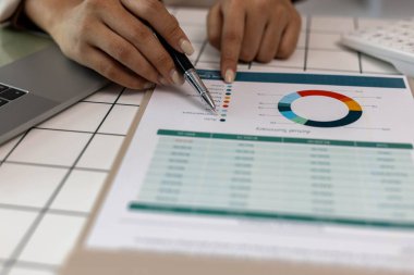 Bir kişi bütçe tablosunu işaret ediyor. Çarşaf yeşil ve beyaz ve üzerinde bir sürü rakam var. Kişi numaraları göstermek için bir kalem kullanıyor.