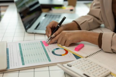 Bir kişi bütçe tablosunu işaret ediyor. Çarşaf yeşil ve beyaz ve üzerinde bir sürü rakam var. Kişi numaraları göstermek için bir kalem kullanıyor.