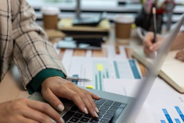 Masasında dizüstü bilgisayarı ve not defteri olan bir kadın oturuyor. Dizüstü bilgisayardaki bir şeyi işaret ediyor.