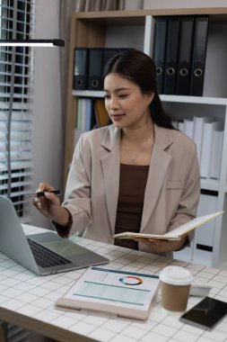 Masasında dizüstü bilgisayarı ve not defteri olan bir kadın oturuyor. Dizüstü bilgisayardaki bir şeyi işaret ediyor.