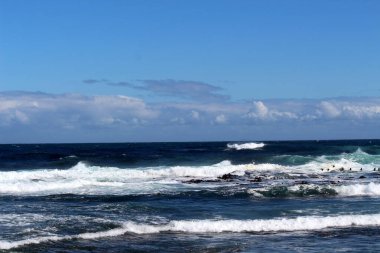 Mavi suyu ve beyaz sörfü olan çalkantılı okyanus.