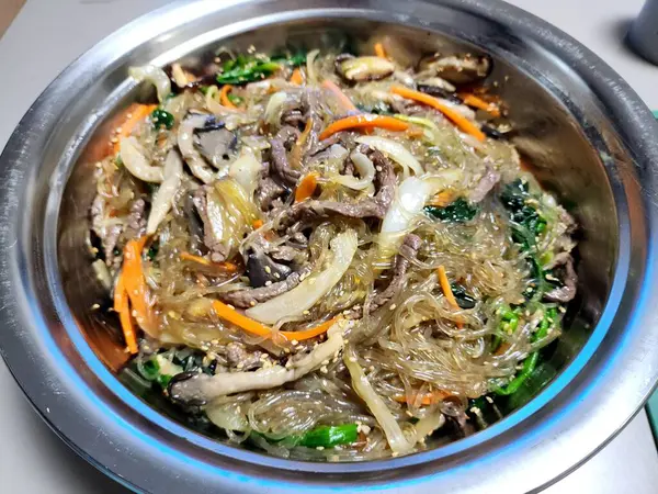 Canlı bir tabak japchae, kızarmış cam şehriye, renkli sebzeler, ve lezzetli soya sosuyla kaplanmış taze et. Klasik bir Kore favorisi.!