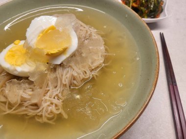 Soğuk ve ferahlatıcı Kore naengmyeon eriştesi, dilimlenmiş salatalık, turp ve haşlanmış yumurta ile servis edilir. Sıcak yaz günleri için nefis, keskin bir yemek..