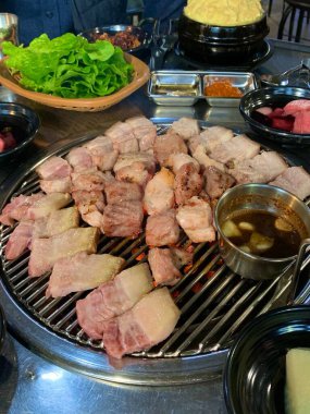 Izgara samgyeopsal, kalın domuz eti dilimleri çıtır çıtır ve taze et. Klasik bir Kore barbekü deneyimi için marul, sarımsak ve sosla servis ediliyor..