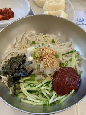 Baharatlı ve keskin bibim guksu, çiğnenmiş erişteler, taze sebzeler ve gochujang sosu. Canlı ve ferahlatıcı bir Kore soğuk erişte tabağı hafif ama lezzetli bir yemek için mükemmel..