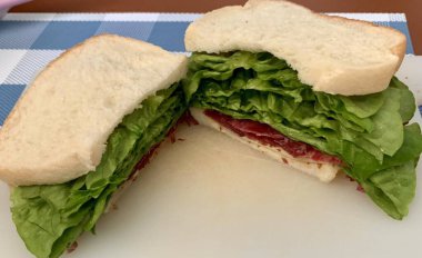 Marul, domates, peynir ve meze gibi taze malzemelerle dolu lezzetli bir sandviç. Hepsi de iki dilim yumuşak ekmeğin arasına istiflenmiş. Hızlı ve tatmin edici bir yemek için mükemmel..