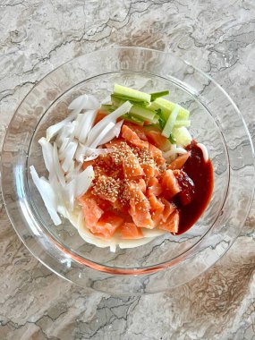 Baharatlı ve keskin bibim guksu, çiğnenmiş erişteler, taze sebzeler ve gochujang sosu. Canlı ve ferahlatıcı bir Kore soğuk erişte tabağı hafif ama lezzetli bir yemek için mükemmel..