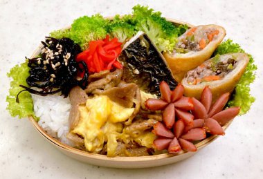 Düzgün düzenlenmiş pirinç, lezzetli protein ve çeşitli mezelerle dolu renkli bir dosirak beslenme çantası. Taşınabilir bir ziyafet, özgün Kore ev usulü yemeklerin özünü yansıtıyor..