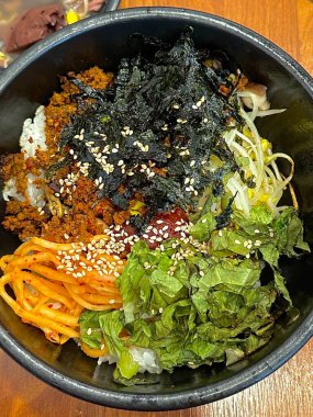 Cızırdayan sıcak dolsot bibibimbap, çıtır pilav, renkli sebzeler, marine edilmiş et, kızarmış yumurta ve gochujang ile servis edilir. Tat ve dokularla dolu bir Kore yemeği..