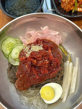 Naengmyeon, üzerine dilimlenmiş sebze, haşlanmış yumurta ve baharatlı sos serpilmiş soğuk Kore erişte tabağı. Yaz yemeği fotoğrafçılığı ve Kore mutfağı projeleri için mükemmel..