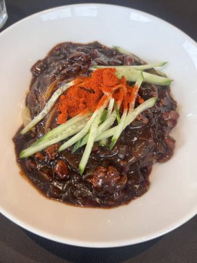 Bir kase jajangmyeon, üzerinde bol siyah fasulye soslu, doğranmış domuz eti ve sebzeler bulunan çiğnenmiş erişteler. Bu ikonik Kore-Çin yemeği lezzetli ve sağlıklı bir lezzet sunuyor..
