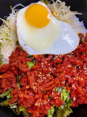 Yukhoe bibimbap taze sebzeler, pilav, baharatlı çiğ biftek, çiğ yumurta sarısı ve Gochujang klasik bir Kore yemeği içinde kalın bir lezzet ve doku karışımı sunar..