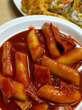 Çiğnenmiş kırmızı soslu pirinç kekleri ve susam tohumları ve yeşil soğanla kaplı baharatlı Kore tteokbokki. Bağımlılık yaratan tadı ve tatmin edici dokusuyla bilinen popüler bir sokak yemeği..