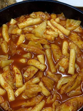 Çiğnenmiş kırmızı soslu pirinç kekleri ve susam tohumları ve yeşil soğanla kaplı baharatlı Kore tteokbokki. Bağımlılık yaratan tadı ve tatmin edici dokusuyla bilinen popüler bir sokak yemeği..