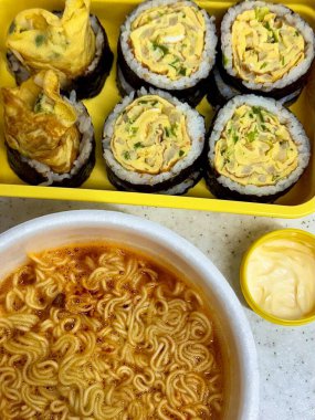 Kimbap ve Ramyun, mükemmel bir Kore karışımı! Lezzetli pirinç rulolarının yanında sebze, et ve turşu ile baharatlı ve rahatlatıcı ramen ye. Günün her saatinde doyurucu bir yemek..
