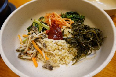 Bibimbap, çeşitli sebzeler, gochujang ve sıklıkla dilimlenmiş etin eşlik ettiği kızarmış yumurta ile süslenmiş canlı bir Kore pirinç yemeği. Karıştırıldığında, aromalı ve dengeli olur..