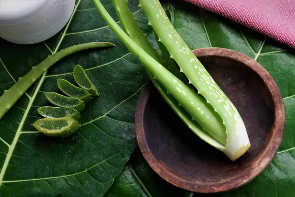 aloe vera yaprakları, ahşap kaseler, ve krem ya da losyon içeren beyaz kavanozlar, büyük yeşil bir yaprağa yerleştirilmiş.