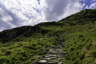 Penygader 'a (Kadair Idris) giden tarihi Minffordd Yolu Snowdonia Ulusal Parkı' ndaki Verdant Slopes ve Dramatik Gökyüzü 'nden yükseliyor