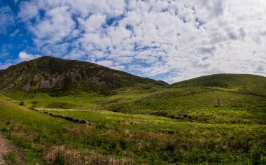 Serene Hills and Verdant Landscapes Near the Start of Minffordd Path to Penygader (Cadair Idris) Under a Sky of Billowing Clouds clipart