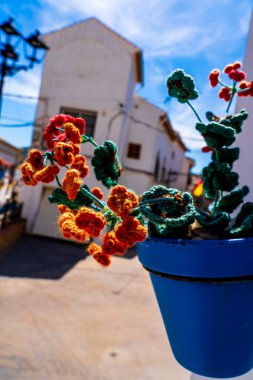 Colorful Crochet Flowers in a Blue Pot with a Quaint Andalusian Village Backdrop clipart