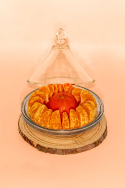 Minimalist natüralizmde cam bir kubbeyle cam bir dilim üzerinde cam bir kasede soyulmuş ve düzenlenmiş portakal bölümleri.