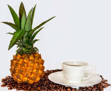 Exotic Mini Pineapple and Elegant White Coffee Cup on a Saucer, Placed on a Bed of Roasted Coffee Beans Against a Clean White Background clipart