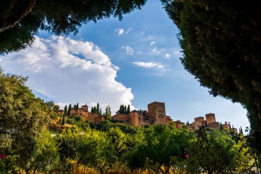Granada 'daki Alhambra Sarayı. Meyve ağaçları ve selvi tarafından çerçevelenmiş. Endülüs gökyüzünün altındaki Fas kulelerini gözler önüne seriyor.