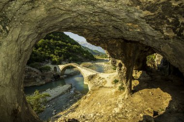 Banje Permet 'teki Ura e Kadiut (Kadiu Köprüsü) adlı kireçtaşı mağarasında, Arnavutluk' un verimli manzarasındaki turkuaz Vjosa Nehri boyunca uzanan bir taş kemer bulunuyor.