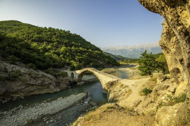 The graceful arch of Ura e Kadiut (Kadiu's Bridge) in Banje Permet arcs across Europes last wild Vjosa River, framed by rugged Albanian green slopes